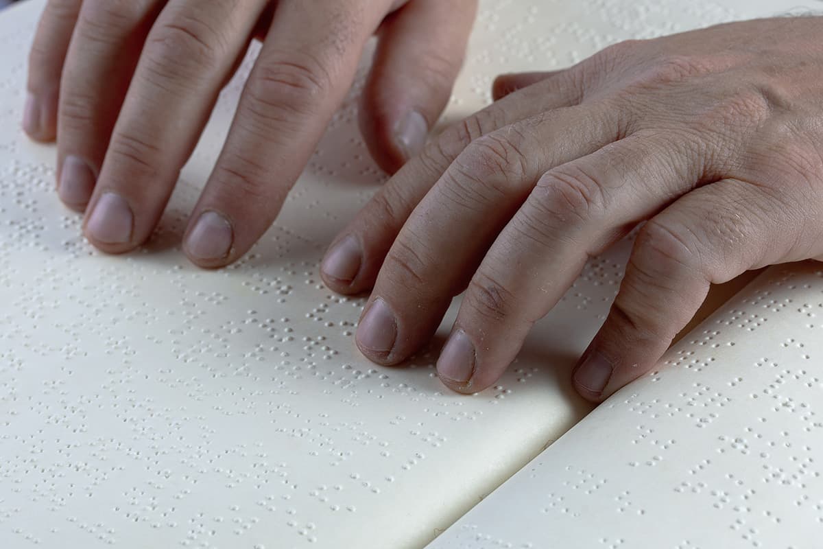 Dita che leggono una pagina in Braille su un libro